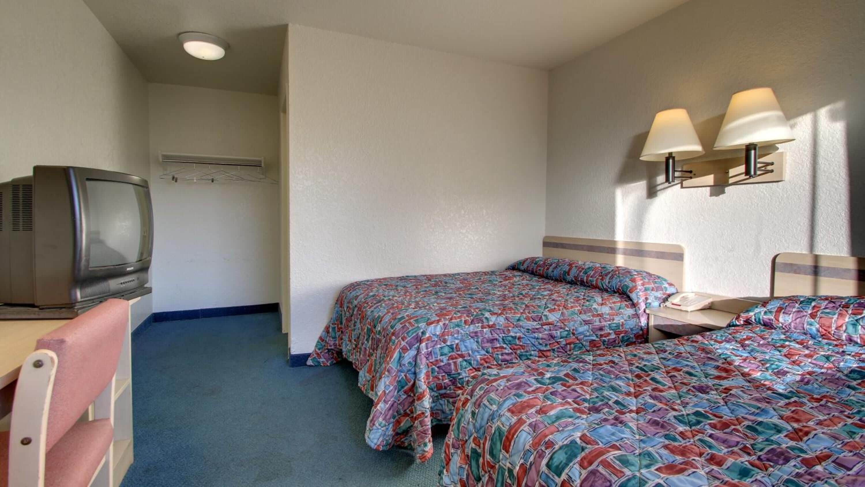 Una habitación de hotel con dos camas, un escritorio con televisor y una lámpara de pared.