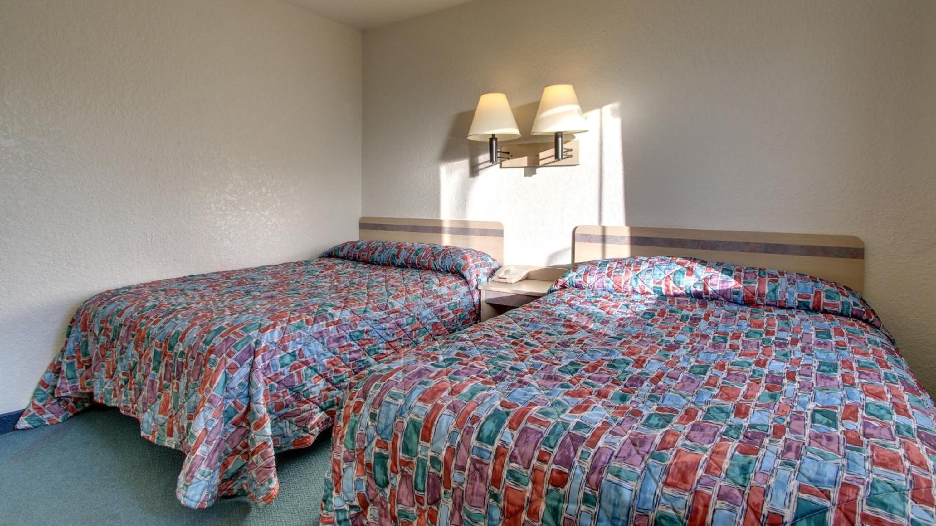 Et hotelværelse med to senge, hver med mønstret sengetøj, et natbord og en lampe monteret på v æggen.
