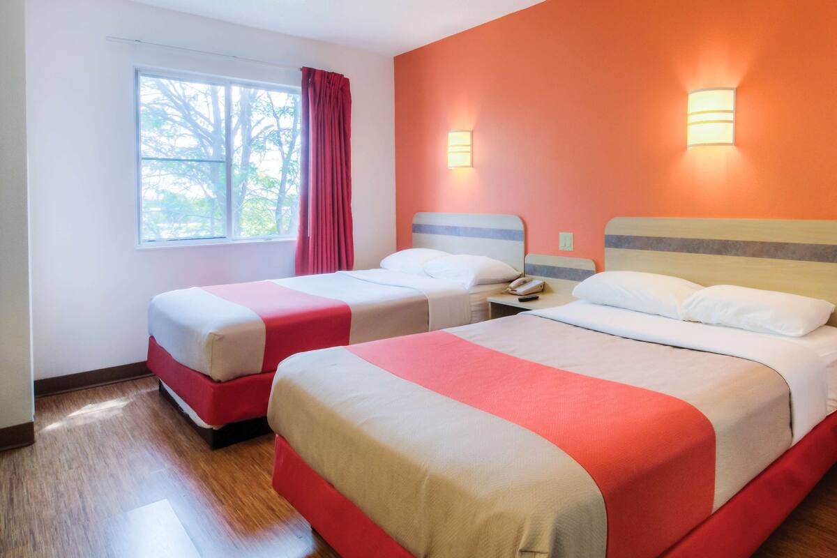 Una habitación de hotel con dos camas, una ventana con cortinas e iluminación en la pared.