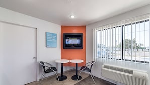 A small room with two tables and chairs, a TV mounted on the wall, and a window with blinds.