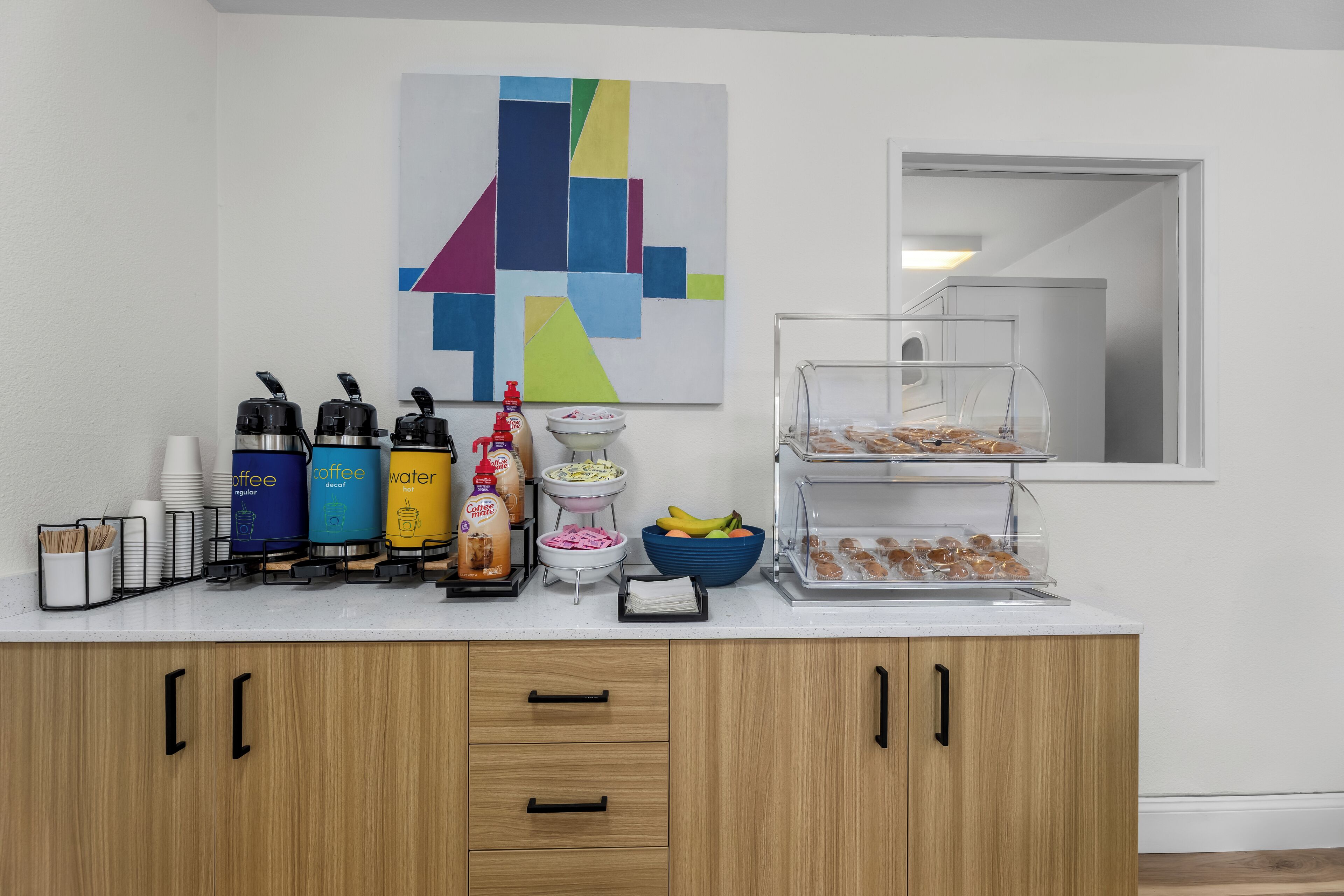 A breakfast bar with coffee dispensers, condiments, and a fruit bowl.
