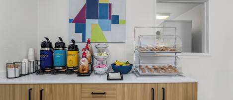 A breakfast bar with coffee dispensers, condiments, and a fruit bowl.