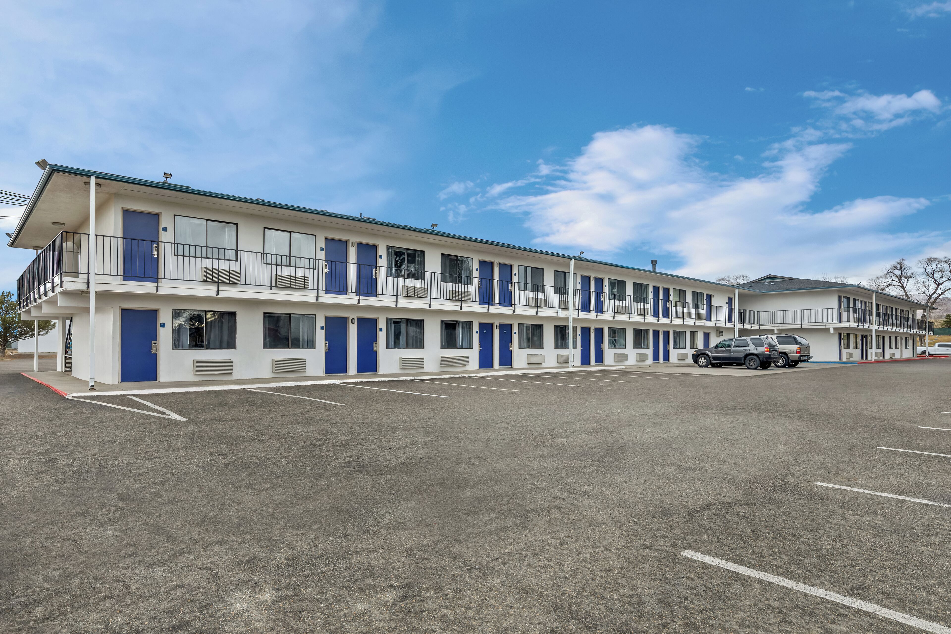 A motel with a row of rooms, a parking lot, and a clear blue sky.