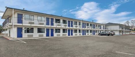 Un motel con una hilera de habitaciones, un estacionamiento y un cielo azul despejado.