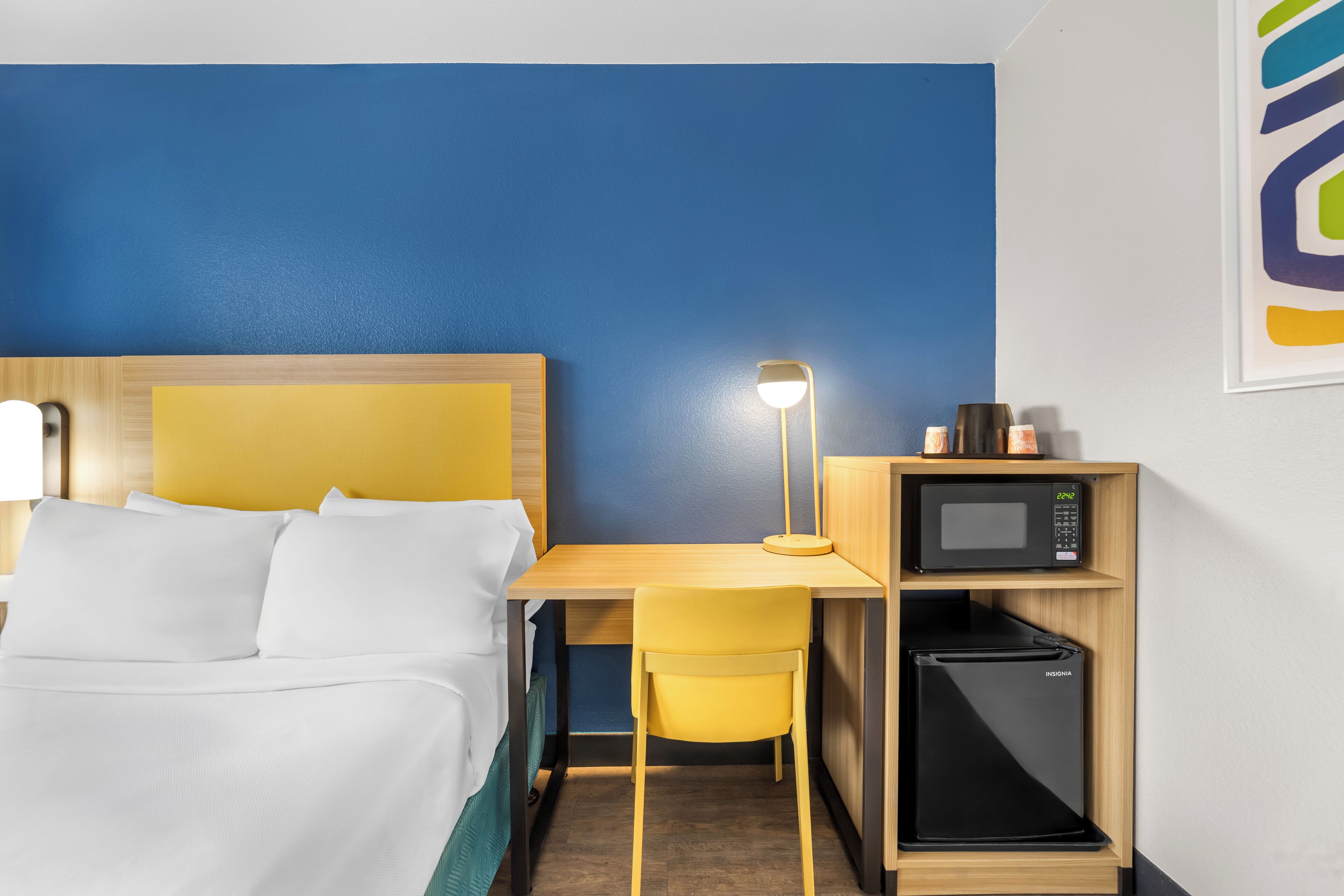 A hotel room with a bed, a desk with a lamp, a microwave, and a refrigerator.