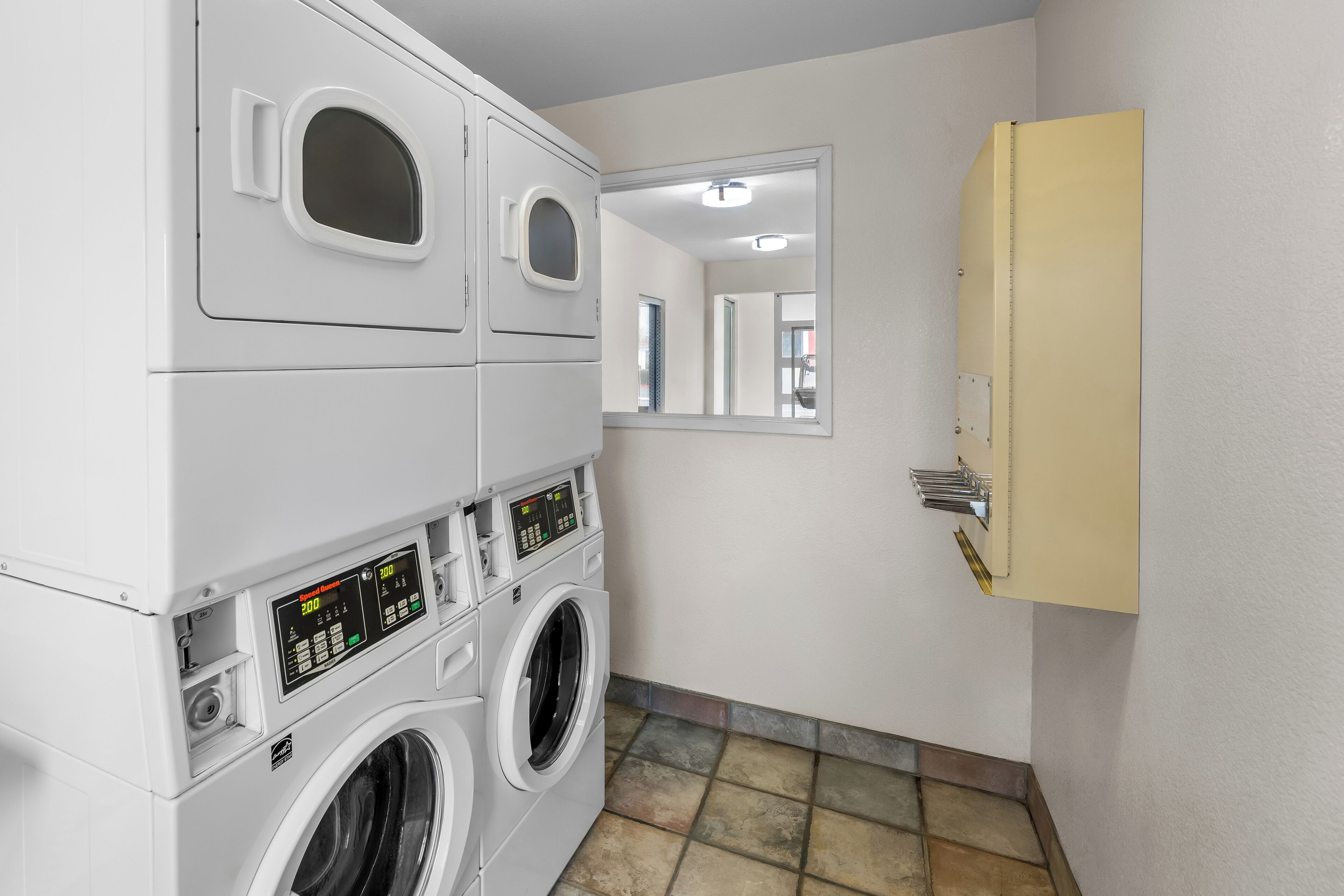 A laundry room with stacked washers and dryers, a mirror, and a cabinet.