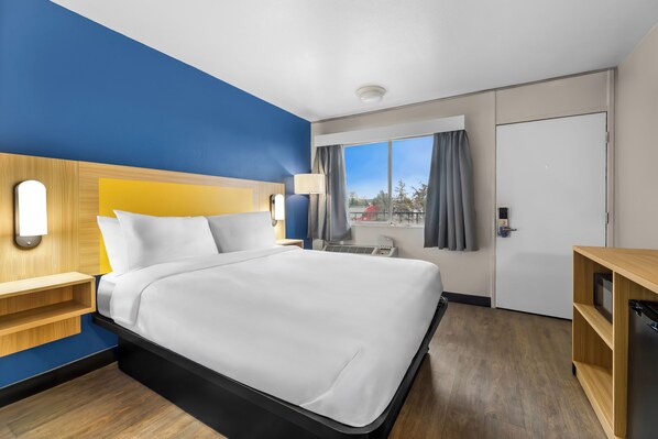 A hotel room with a bed, a desk, a lamp, a window with curtains, and a door. - Park Inn Winnemucca (Winnemucca)