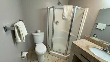 Un baño con inodoro, cabina de ducha de vidrio y lavamanos con espejo.