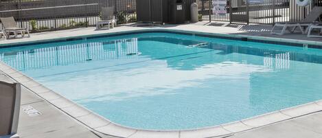 A swimming pool with lounge chairs and a fence.