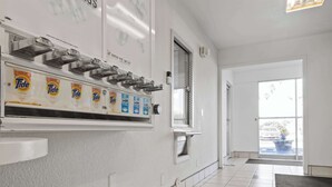 A clean, modern hotel lobby with a Tide detergent dispenser, a window with a view of the parking lot, and a door leading outside.