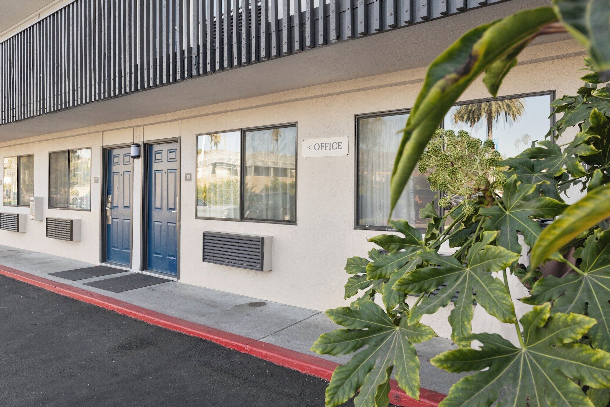 Un bâtiment avec une porte bleue, une enseigne indiquant qu’il s’agit d’un bureau, et une plante au premier plan.