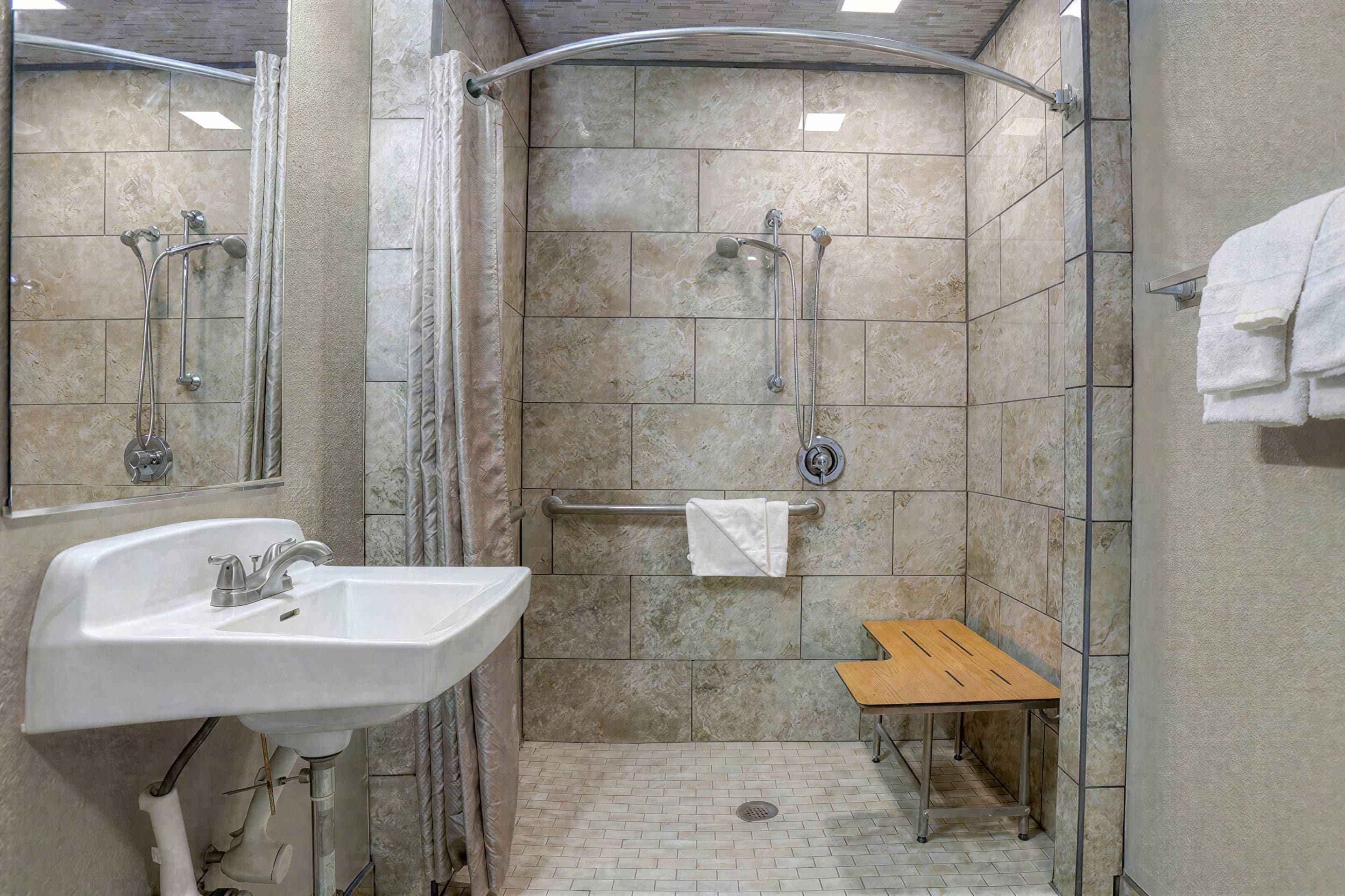 Un espace douche équipé d’un lavabo, d’un porte-serviettes et d’un petit banc en bois.