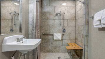 A shower area with a sink, a towel rack, and a small wooden bench.