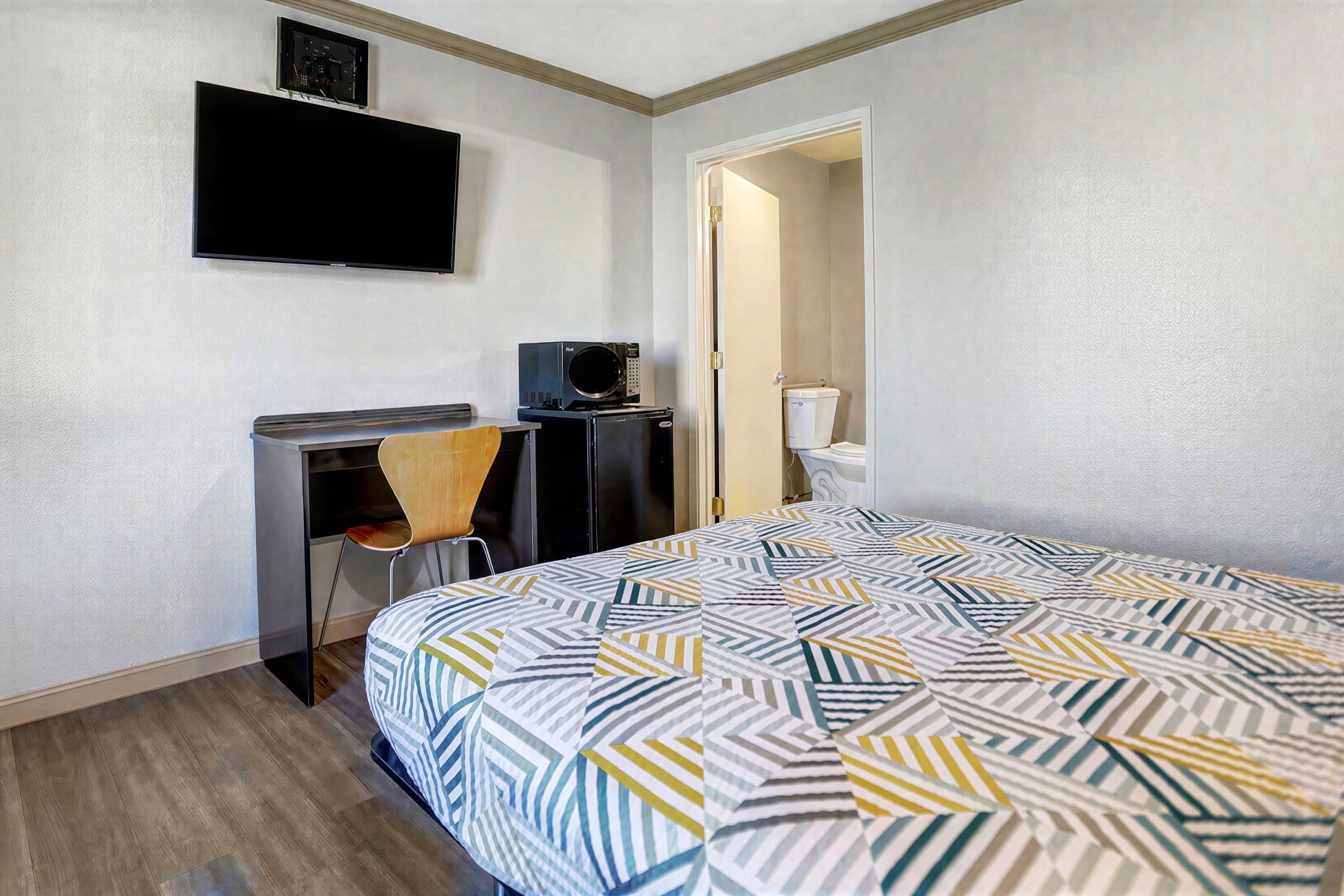 Une chambre d’hôtel comprenant un lit, un bureau avec une chaise, un téléviseur fixé au mur et une porte donnant accès à une salle de bain.