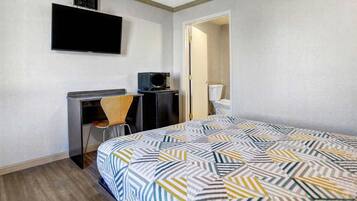 Une chambre d’hôtel comprenant un lit, un bureau avec une chaise, un téléviseur fixé au mur et une porte donnant accès à une salle de bain.