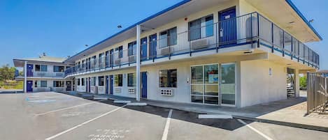 A multi-story motel with a parking lot, featuring a flat roof and a balcony on the second floor.