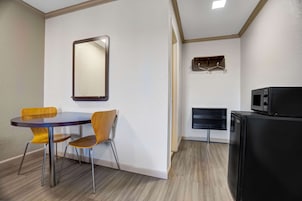 Una habitación compacta con una mesa redonda y dos sillas, un refrigerador negro, un microondas y un espejo en la pared.