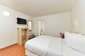 A hotel room with a bed, a TV mounted on the wall, a wooden shelf, a mirror, and a light fixture. - Anderson Inn (Anderson)