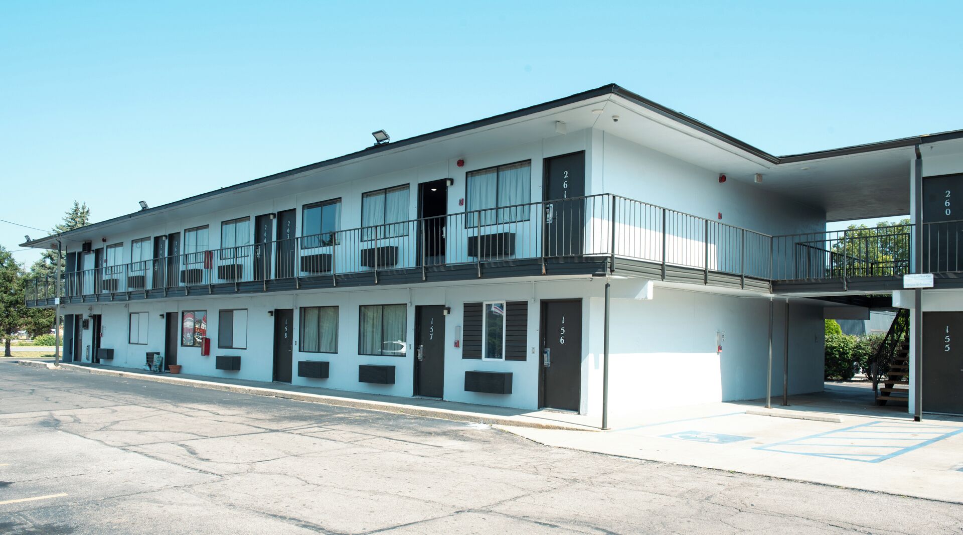 Un motel de dos pisos con habitaciones numeradas, zona de estacionamiento techada y cielo despejado.