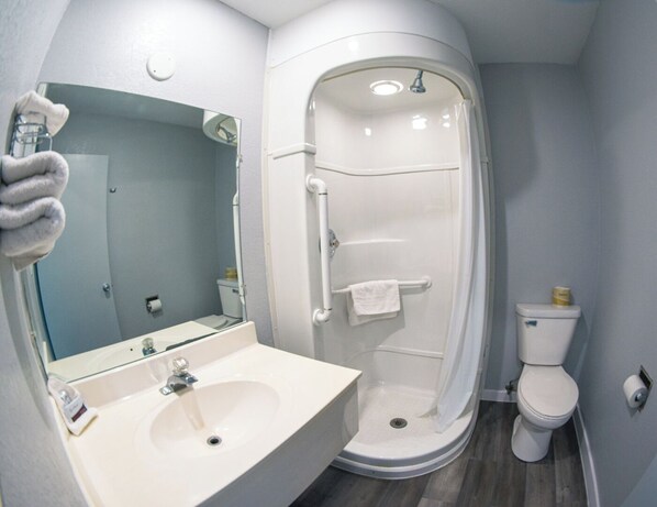 A modern bathroom with a white sink, mirror, and shower. - Anderson Inn (Anderson)