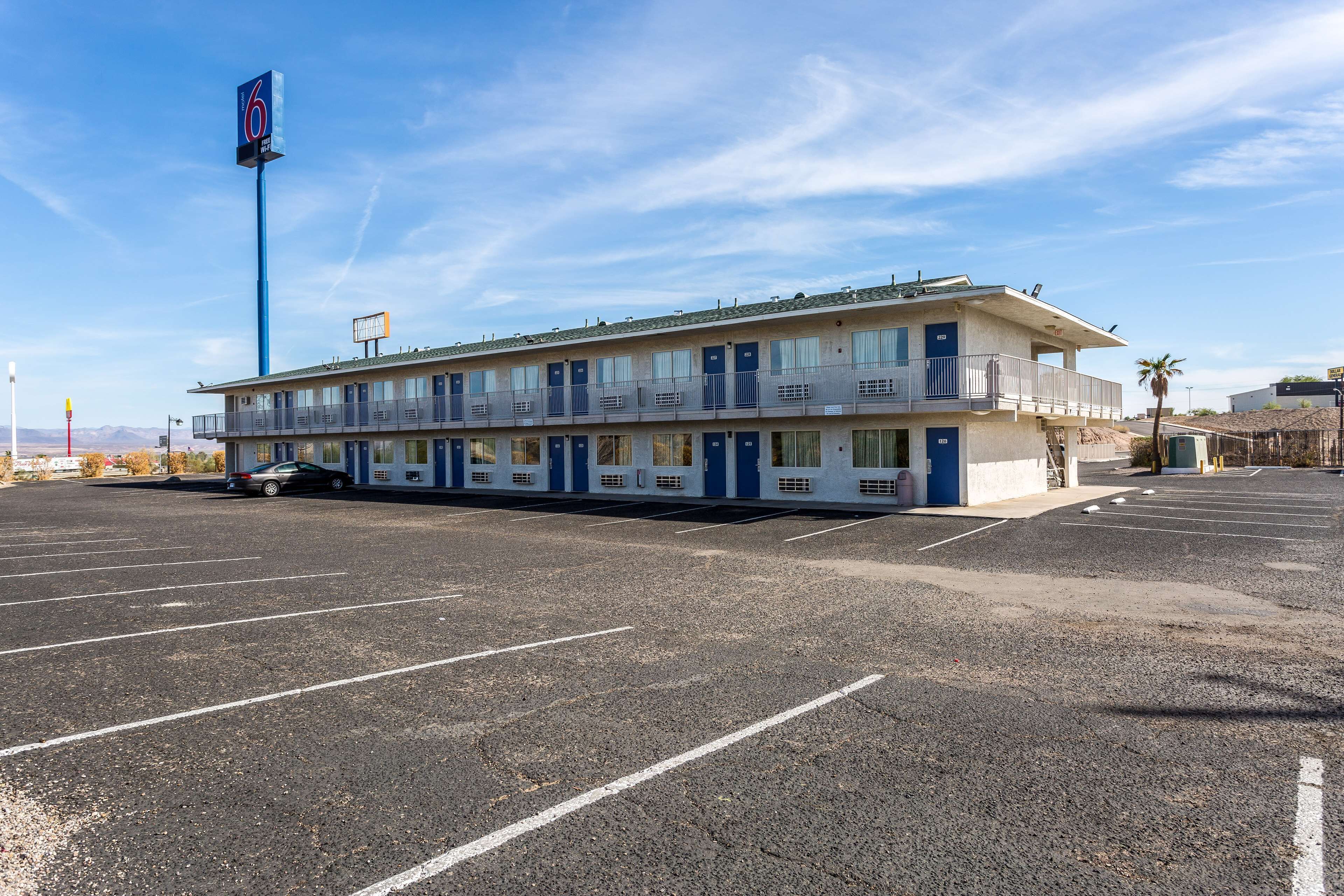 Un motel con una hilera de habitaciones, un estacionamiento y cielo despejado.