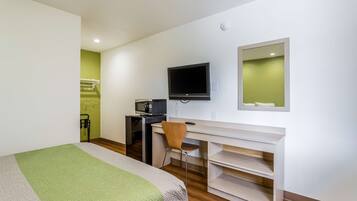 A hotel room with a bed, a desk with a TV, a chair, and a small kitchenette.