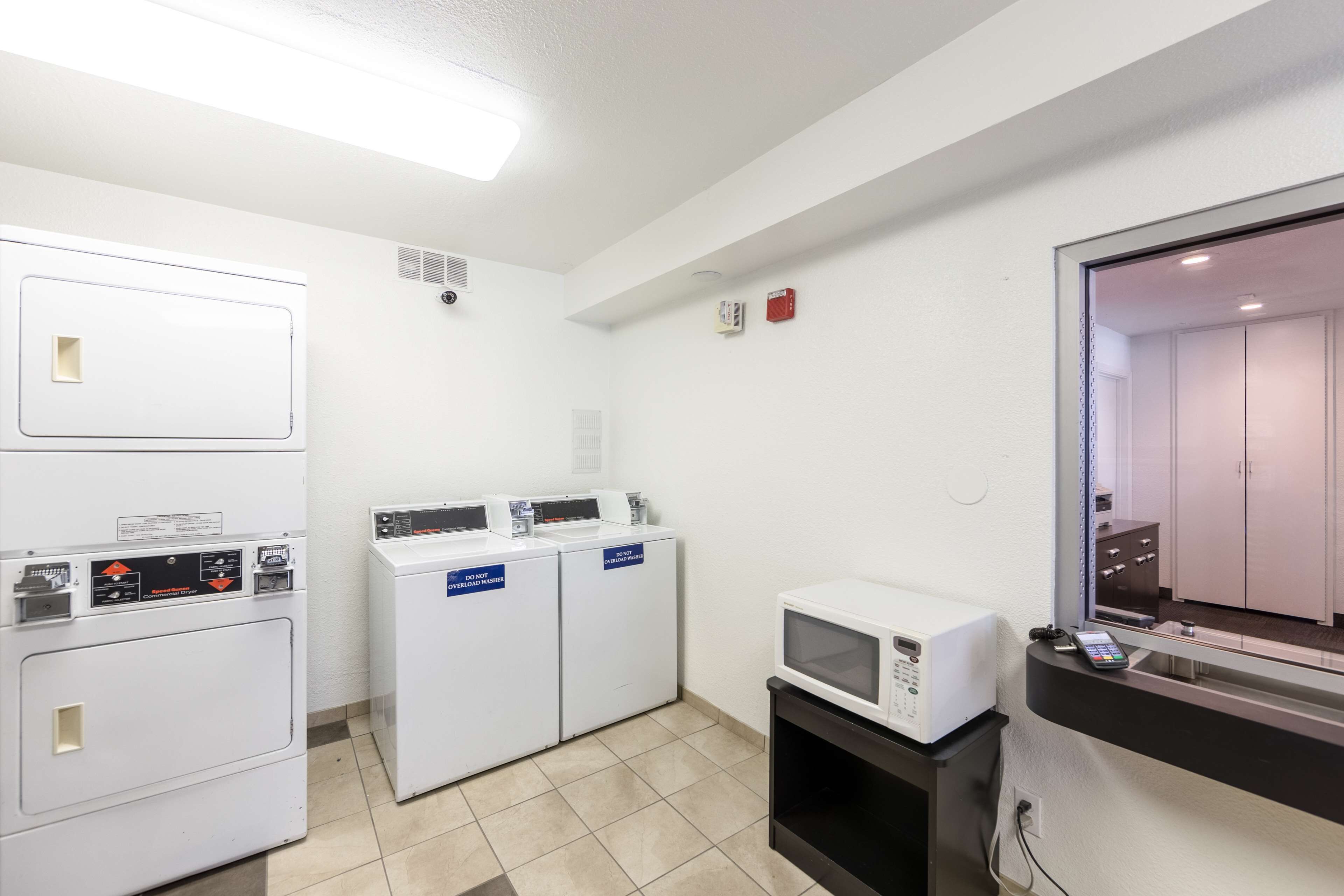 A laundry room with stacked washers and dryers, a microwave, and a small cabinet with a phone.