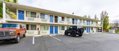 Un motel composé d’un bâtiment à deux étages, de plusieurs chambres avec des portes bleues et d’un parking où sont stationnés deux véhicules.