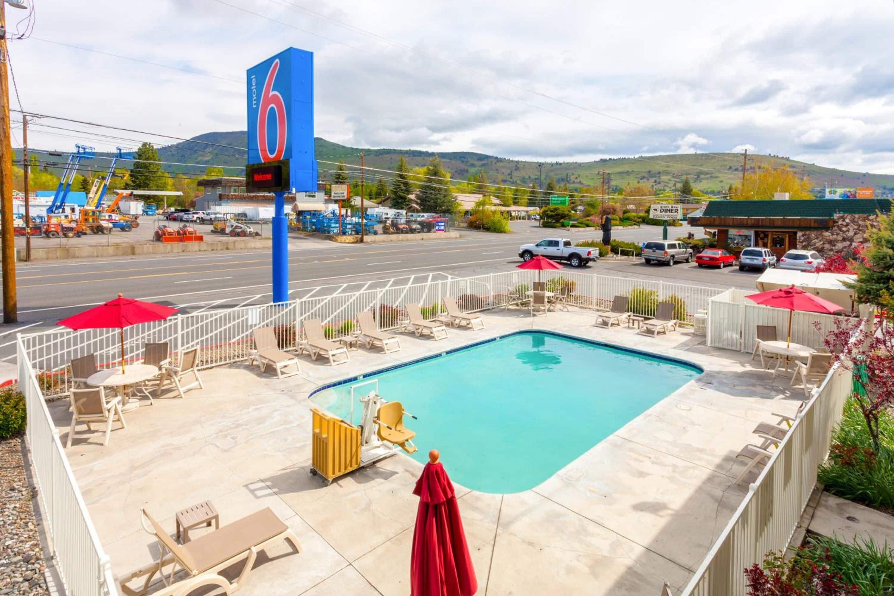 A motel with a swimming pool, outdoor seating, and a view of the surrounding area.