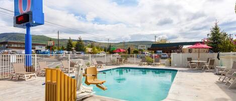A motel with a pool area, including lounge chairs and a lifeguard chair.