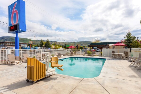 A motel with a pool area, including lounge chairs and a lifeguard chair.