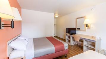 A hotel room with a bed, a desk, a chair, a TV, and a lamp.