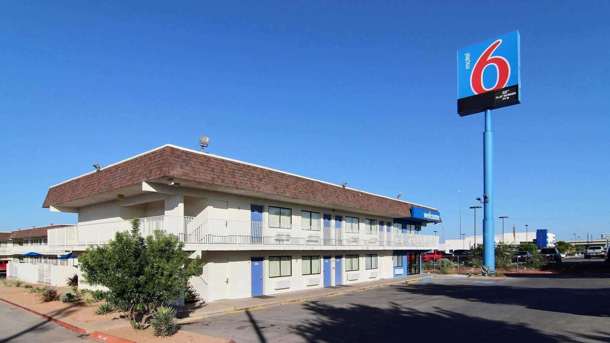 Um motel com uma grande placa indicando a quarto número 6, apresentando um edifício de dois andares com telhado plano e um anexo térreo.