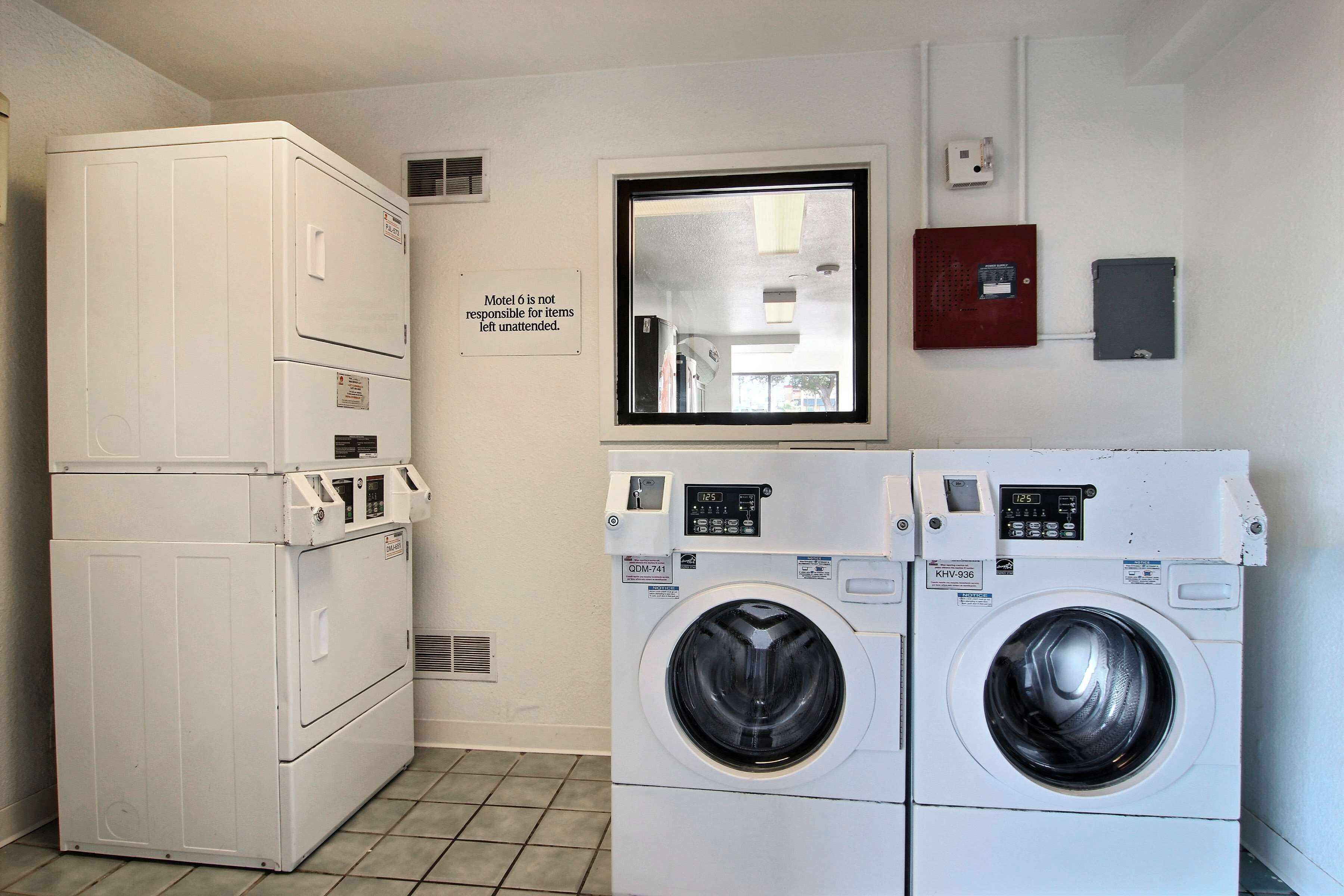 A laundry room with a stacked washer and dryer, a sign indicating room 6 is not responsible for unattended items, and a fire alarm box on the wall.