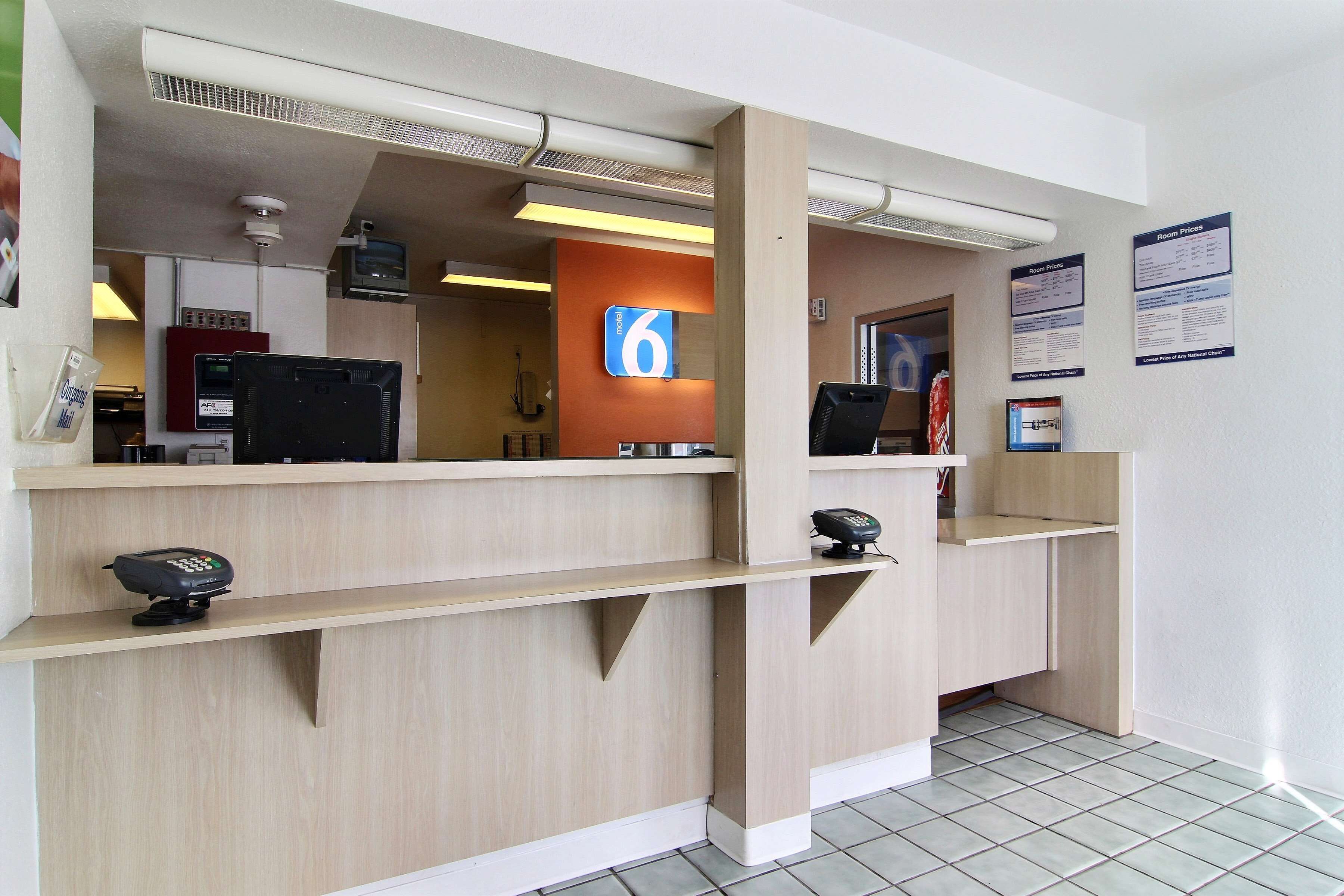 Een hotel receptie met een houten balie, een digitaal scherm en een bord met kamer nummer 6.