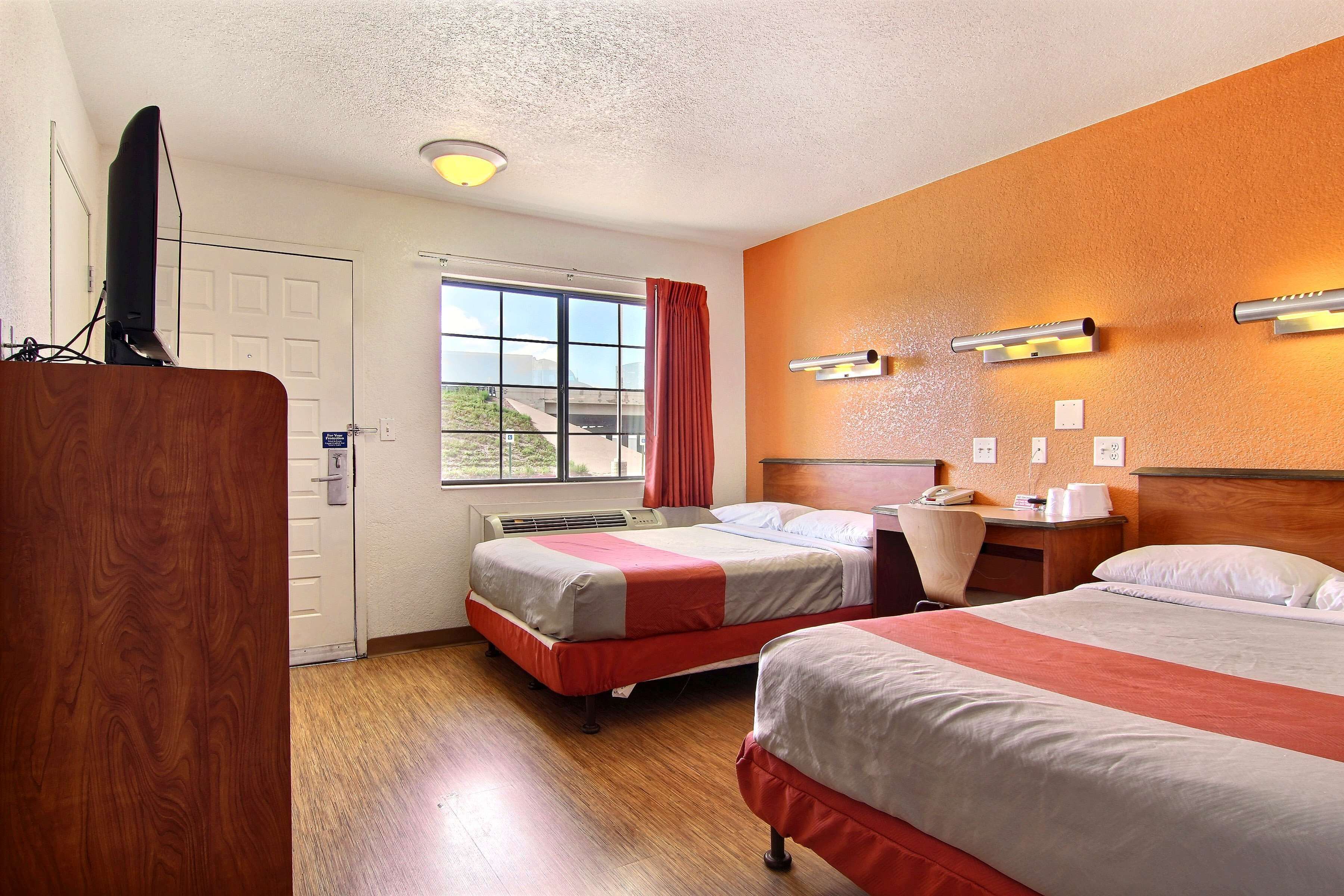 A hotel room with two beds, a desk, a chair, and a television.