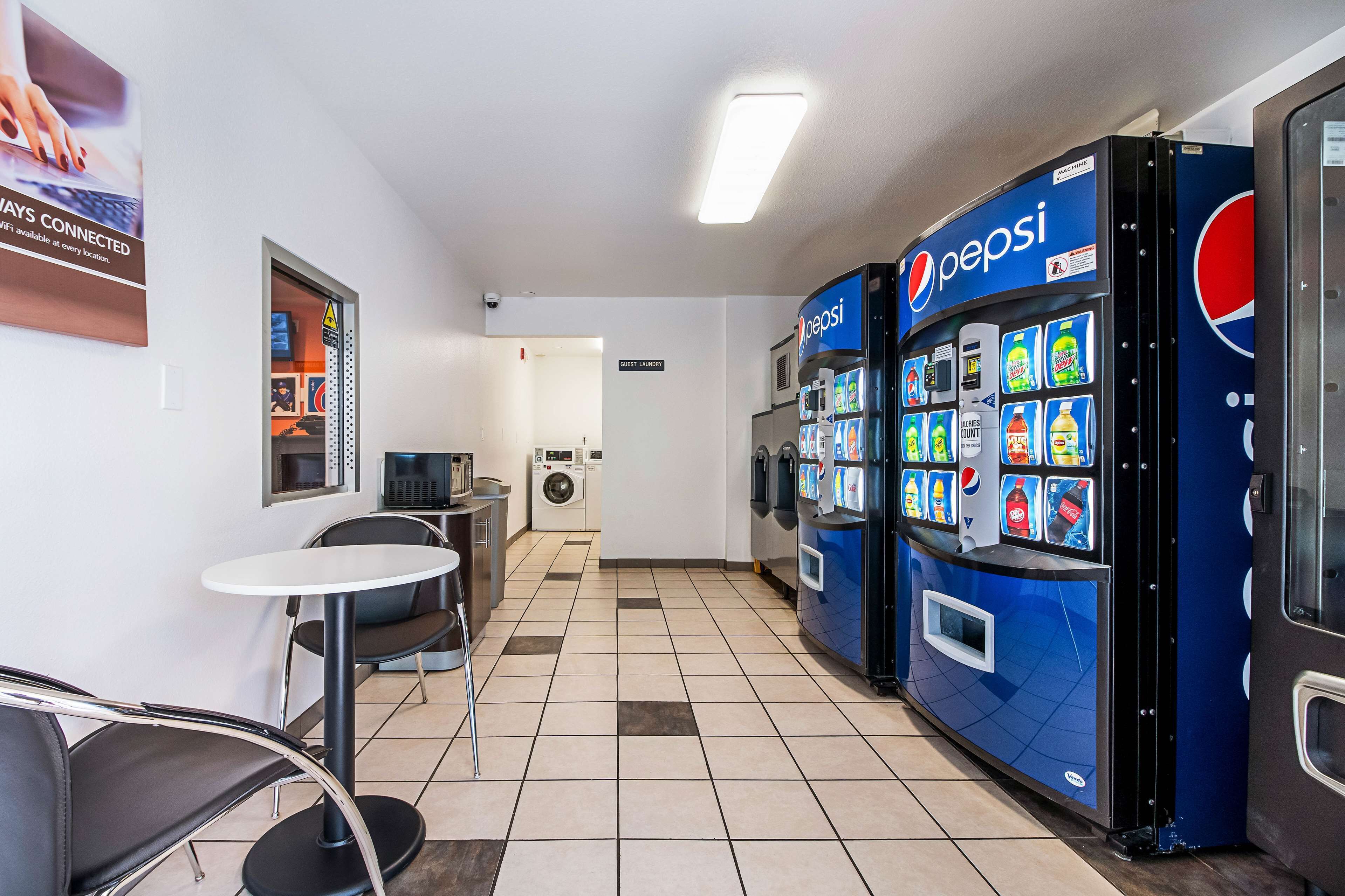 Een schone, moderne hotellobby met een automaat voor Pepsi, een klein zitgedeelte en een wasserette op de achtergrond.