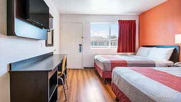 A hotel room with a desk, two beds, a TV mounted on the wall, and a window with curtains.