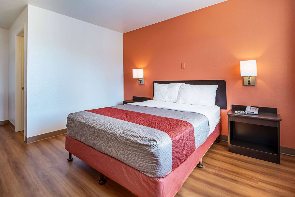 A hotel room with a bed, two bedside tables, and two wall-mounted lamps.
