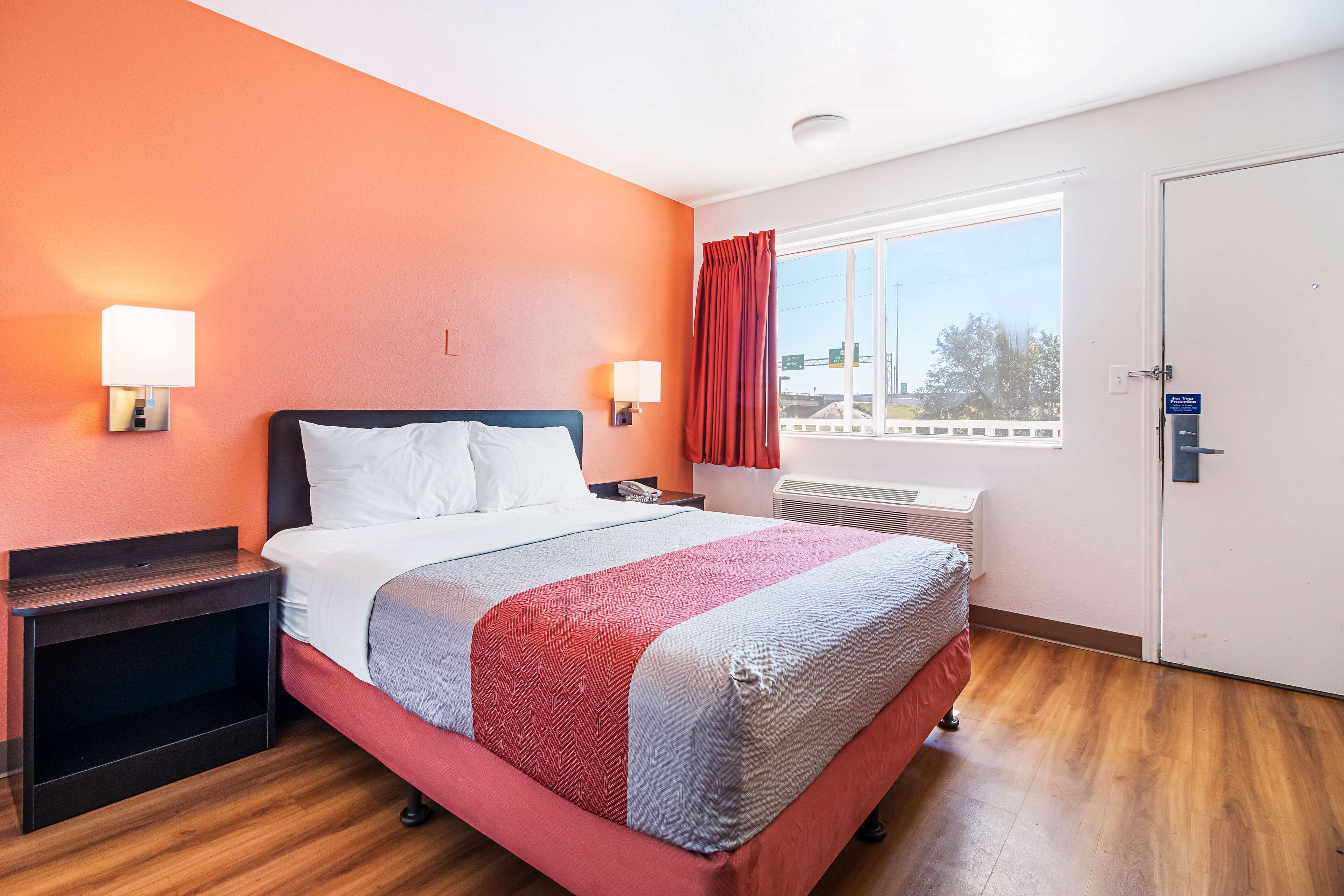 A hotel room with a bed, nightstands, a window with curtains, and a door.