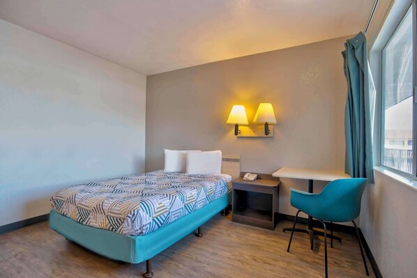 Ein Hotelzimmer mit einem Bett, einem Schreibtisch mit Telefon, einem Sessel und zwei Wandleuchten.