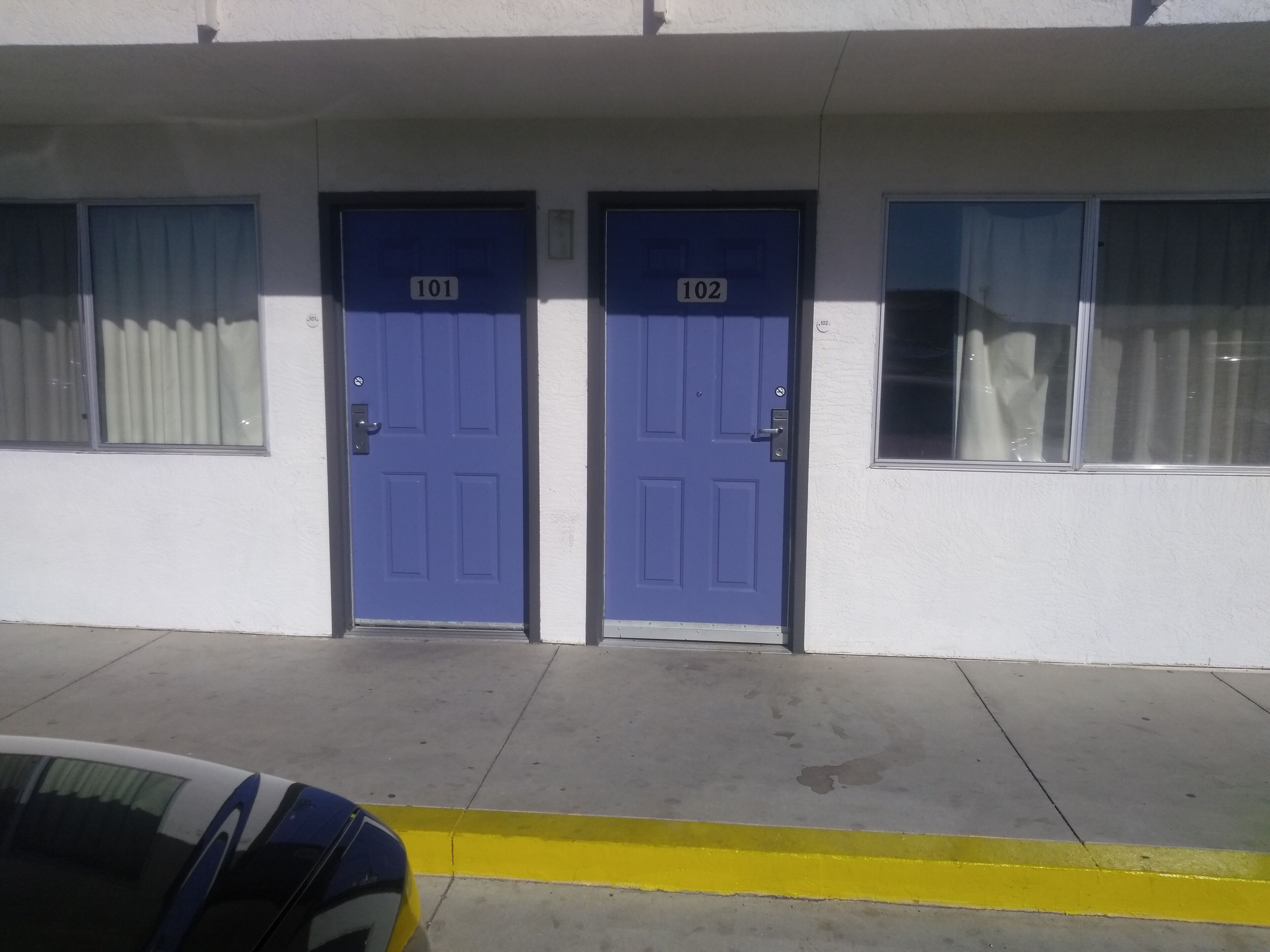A building with two doors labeled 101 and 102, a yellow curb, and a parked car.