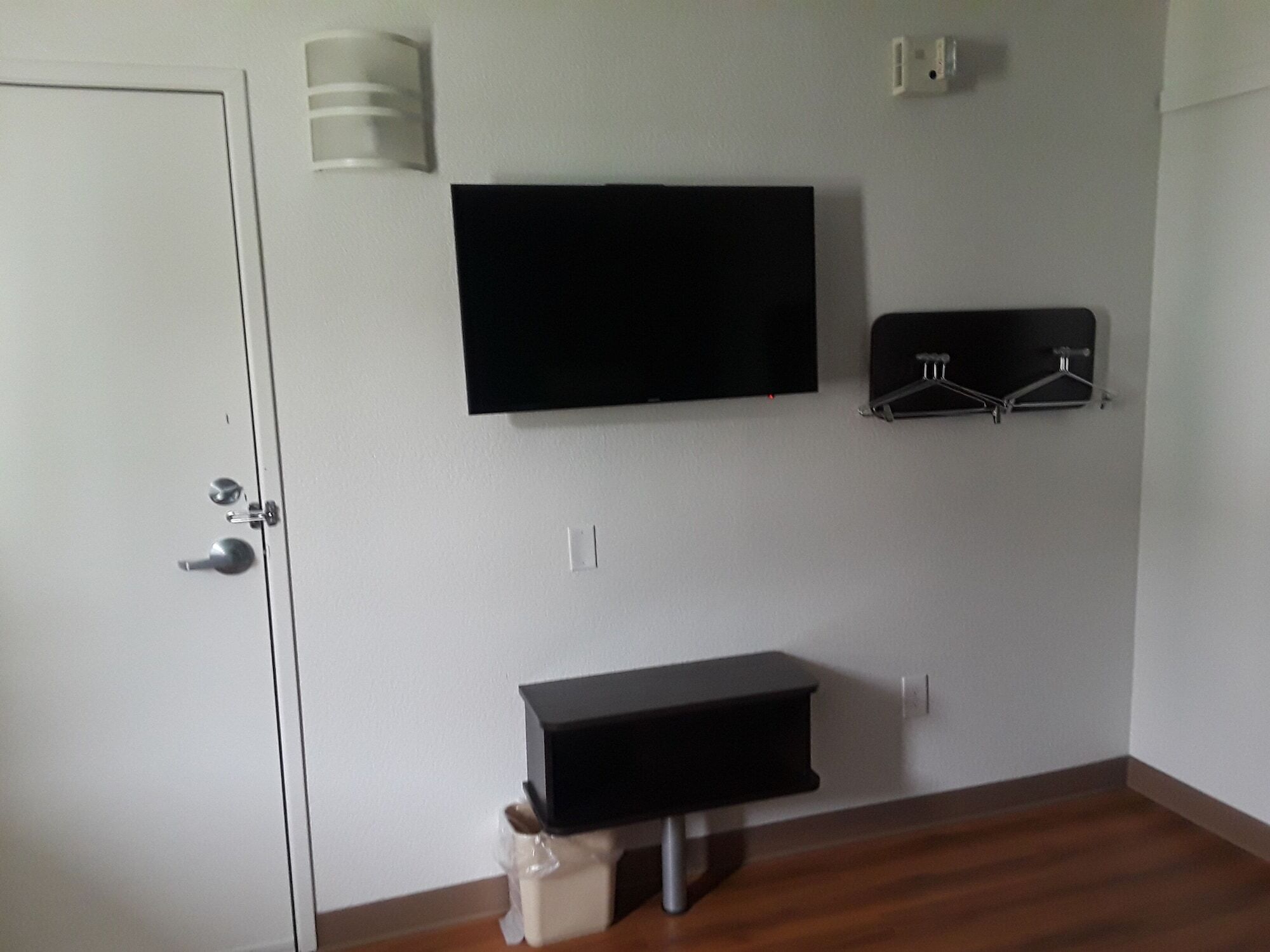 A room with a door, a mounted TV, a coat rack, and a small table.