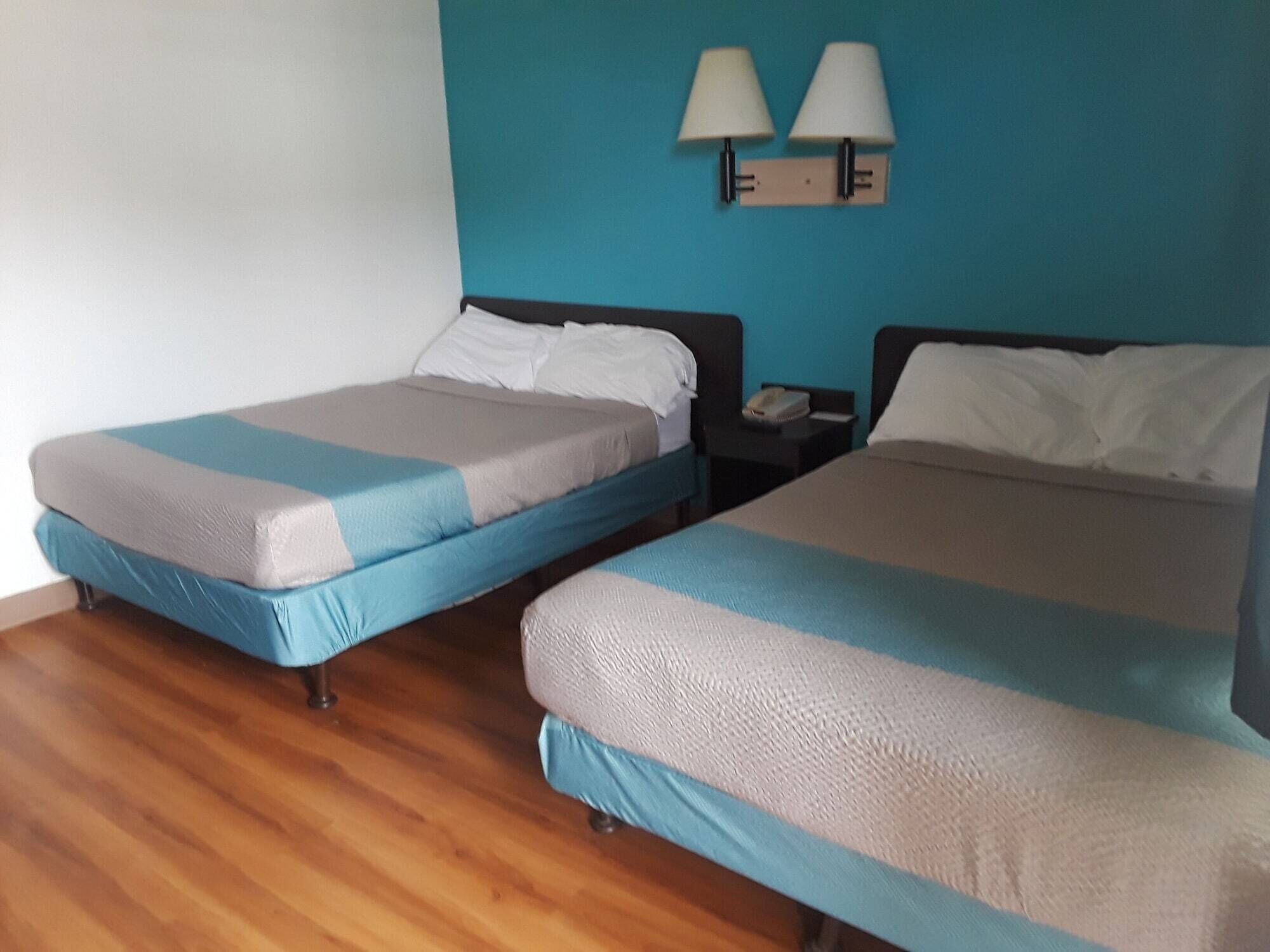 Two single beds with blue and grey bedding, a wooden floor, and a wall-mounted lamp.