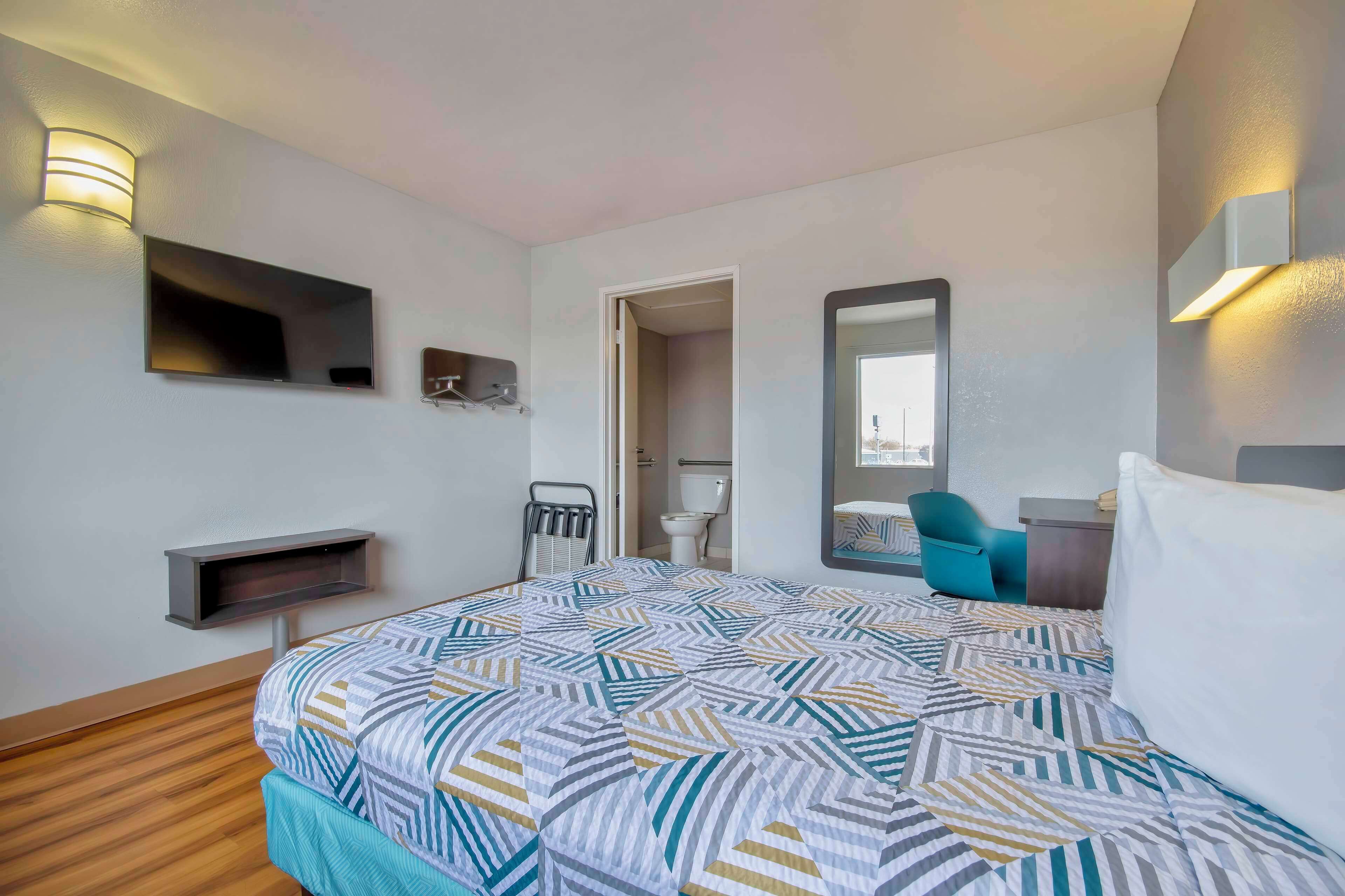 A hotel room with a bed, a TV, a mirror, a chair, and a small desk.