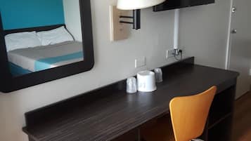A hotel room with a bed, a desk with a chair, a TV mounted on the wall, and a trash bin.