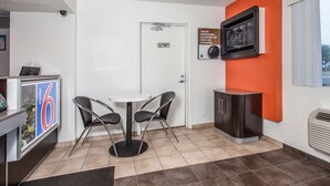 A hotel room with a white door, a minibar, a television mounted on the wall, and a small table with two chairs.