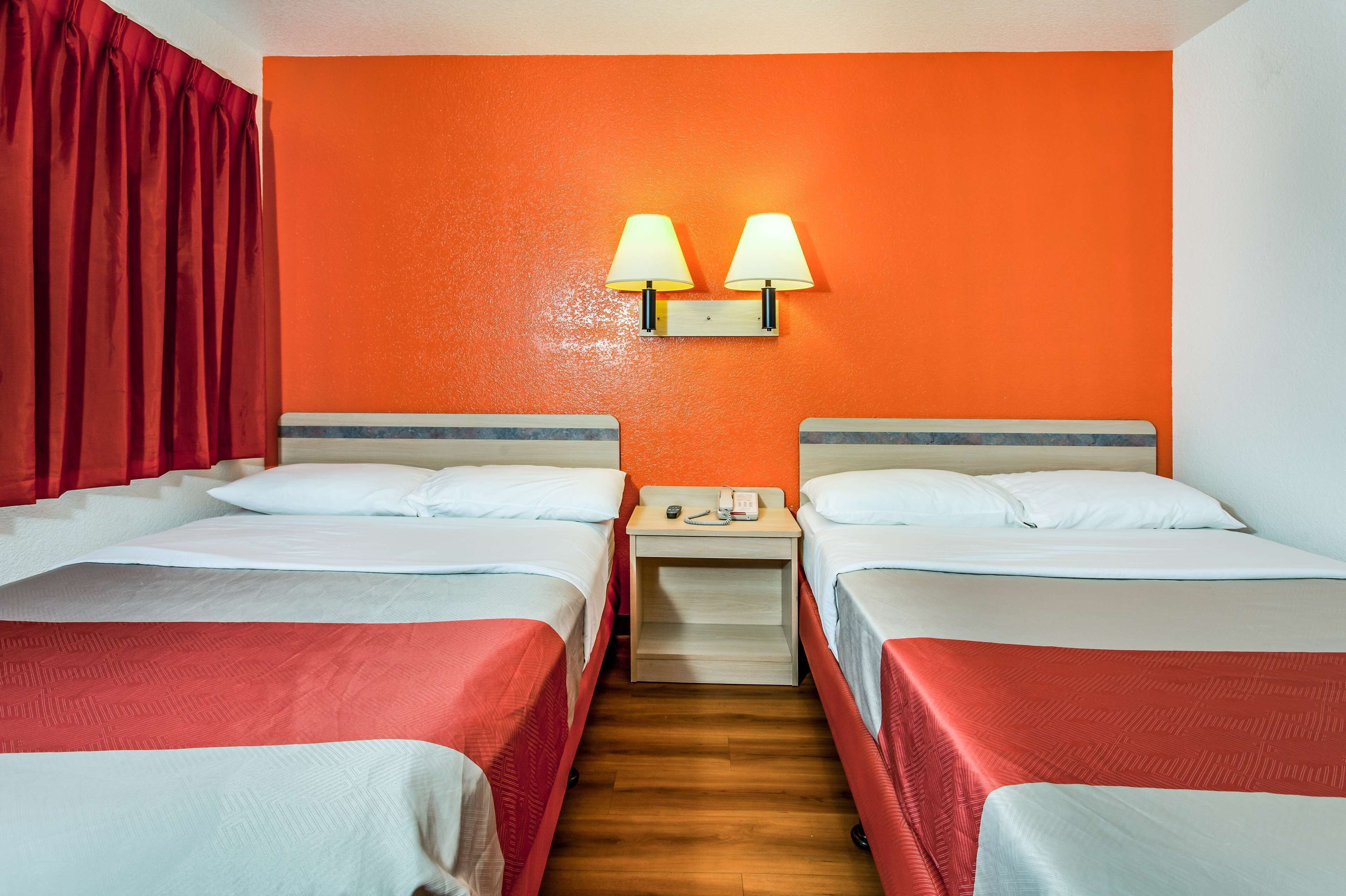 Habitación de hotel con dos camas, una mesita de noche de madera y dos lámparas de pared.