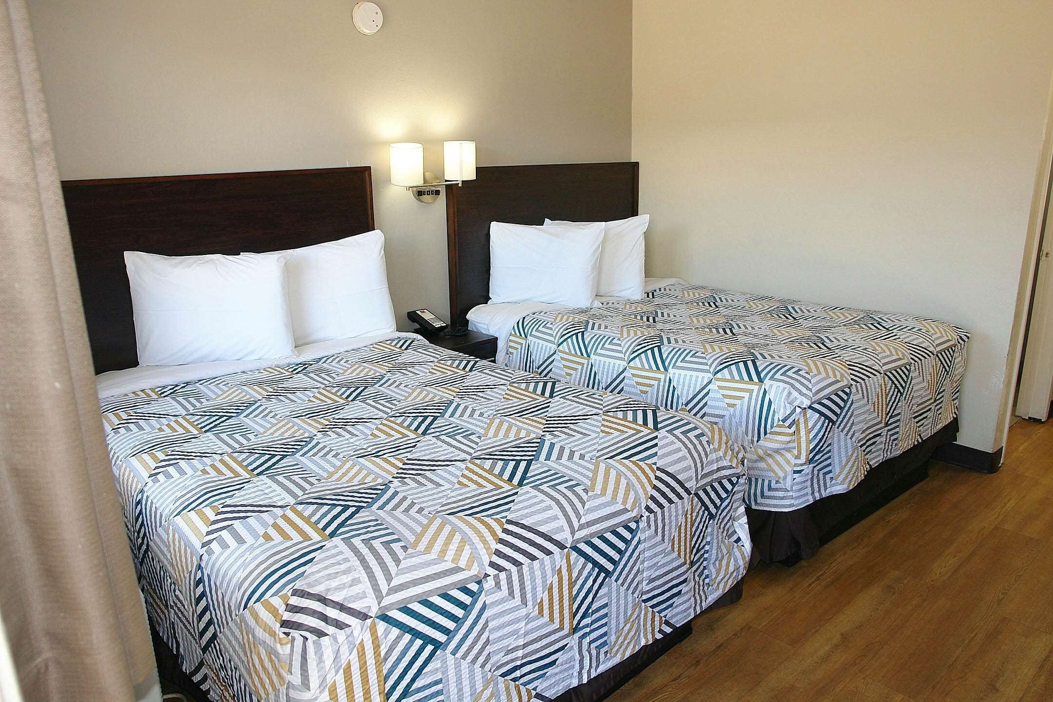 Two single beds with patterned bedding, a nightstand with a phone, and wall-mounted lamps.