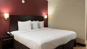 A hotel room with a large bed, two bedside tables, a nightstand, and wall-mounted lamps. - Motel 6 Hattiesburg, MS (Hattiesburg)